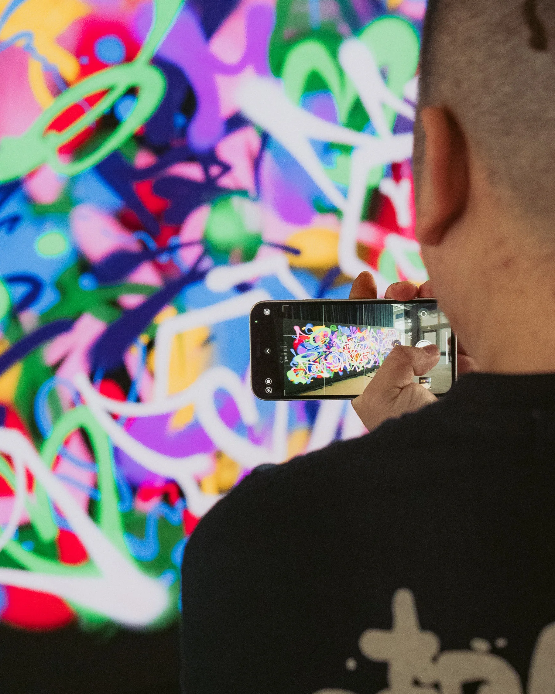 Visitor photographing a finished vivid abstract graffiti piece on the Graffiti+ wall at MGM Cotai