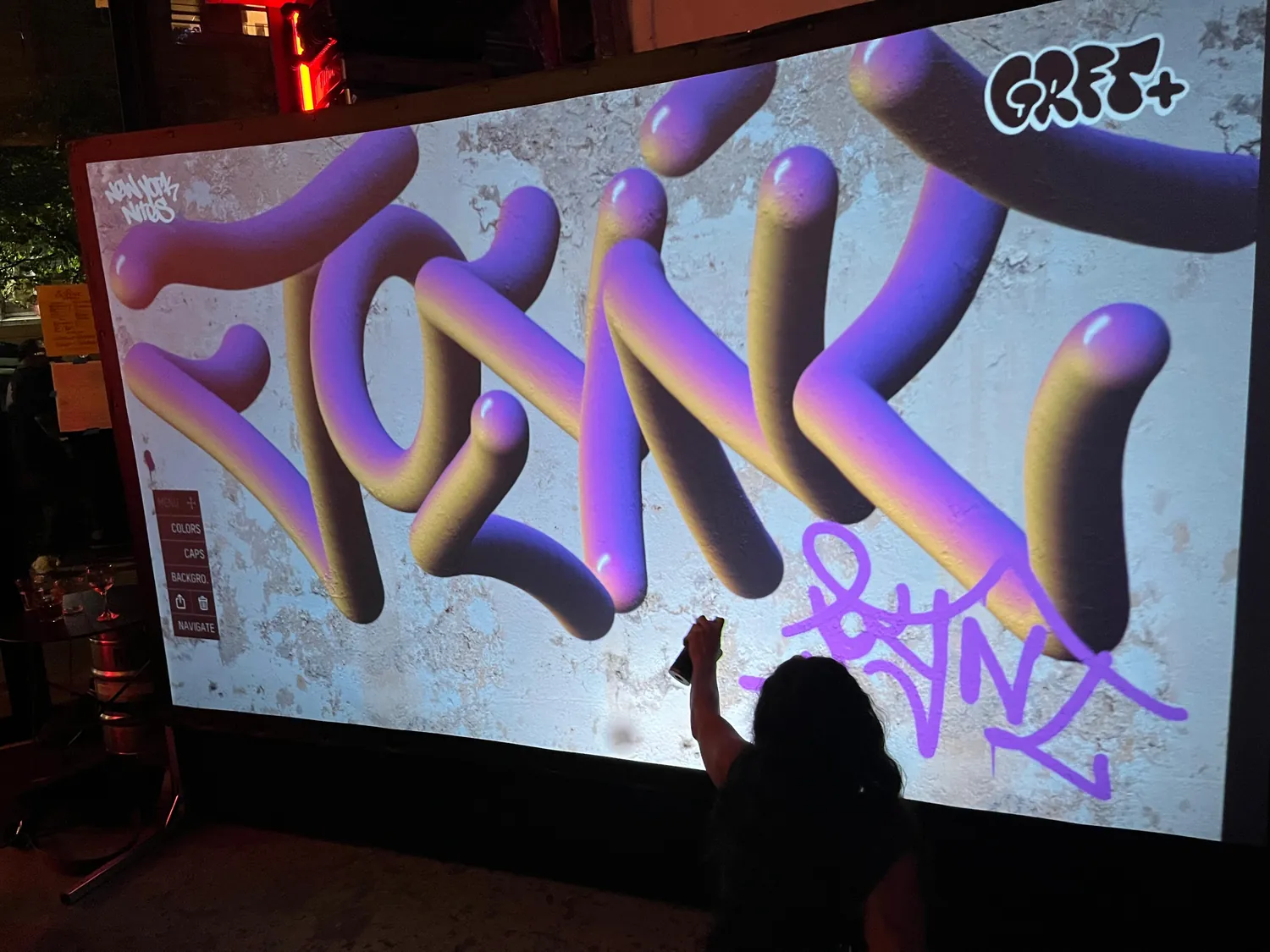 A live piece going up on the Graffiti+ wall as the crowd looks on