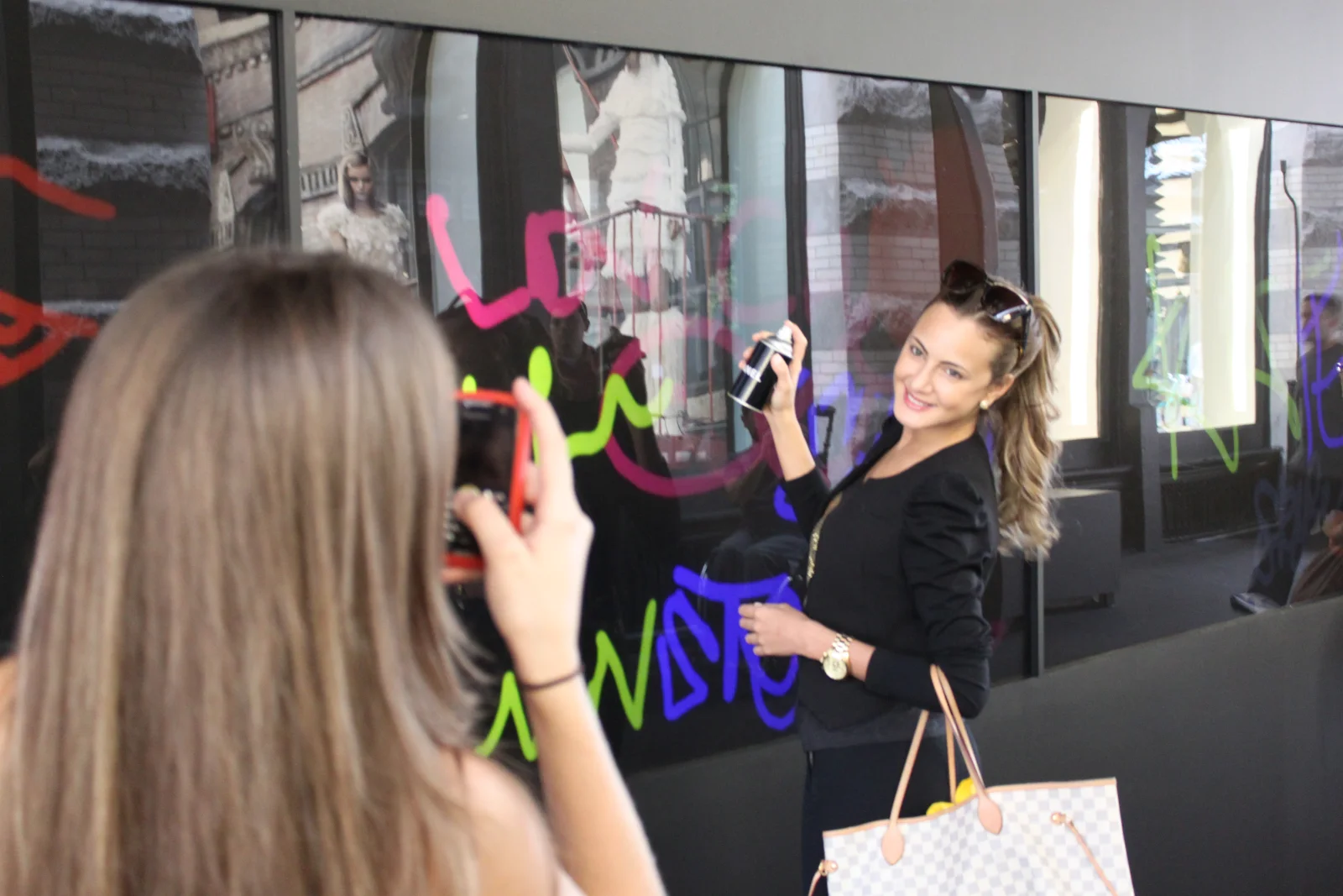 A guest spray-painting colourful graffiti on the Chanel SoHo storefront LED screens with a Chanel-branded can while a friend photographs her, Fashion's Night Out 2010