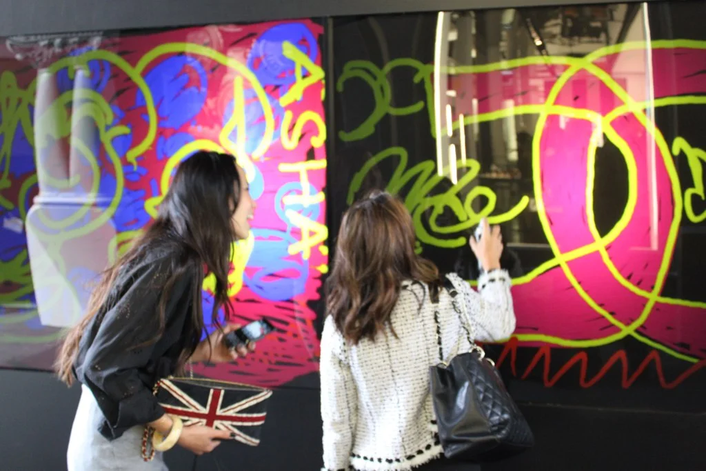 Two guests — one in a Chanel tweed jacket with a Chanel quilted bag — painting bright graffiti on the storefront LED wall at the Chanel SoHo reopening, 2010
