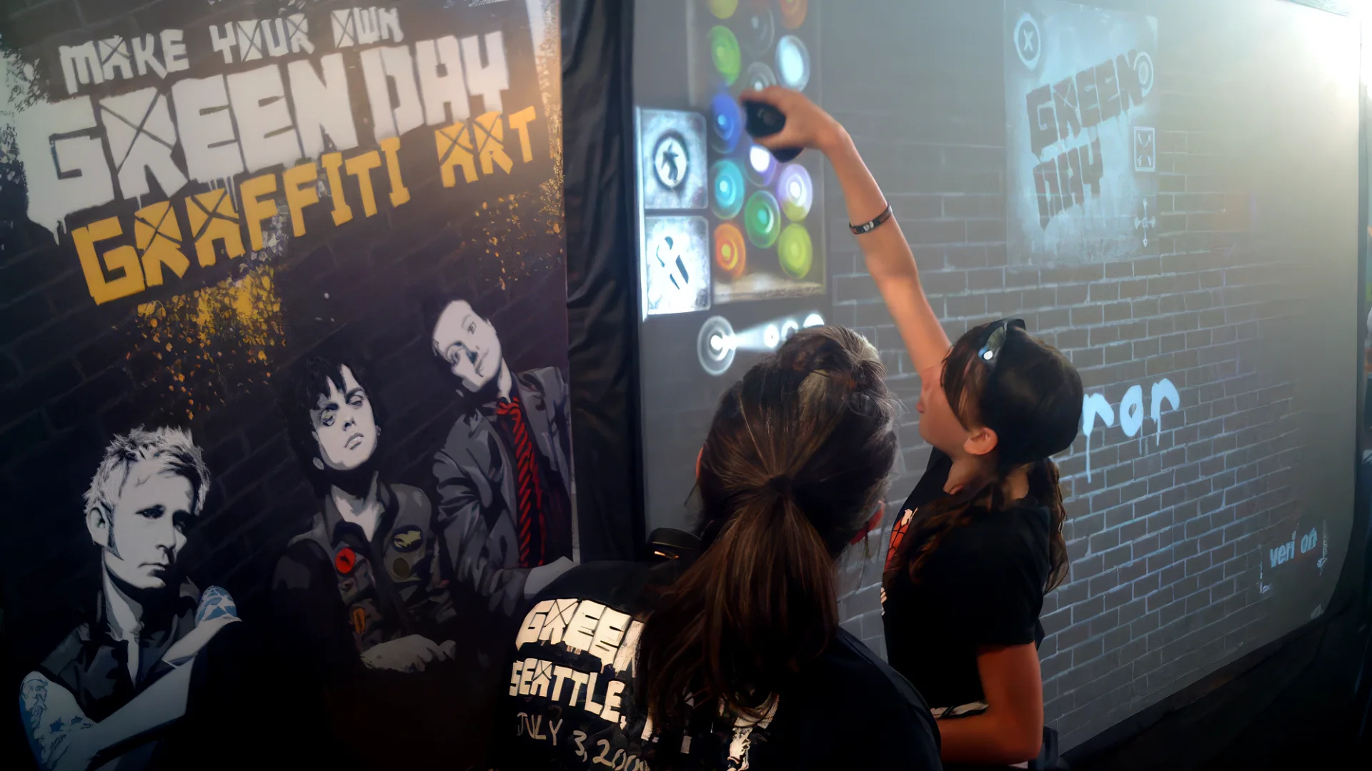 Two fans at the Make Your Own Green Day Graffiti Art wall on the 21st Century Breakdown tour — one spraying with the colour palette and Green Day stencils on the digital wall, the band poster and Verizon branding alongside