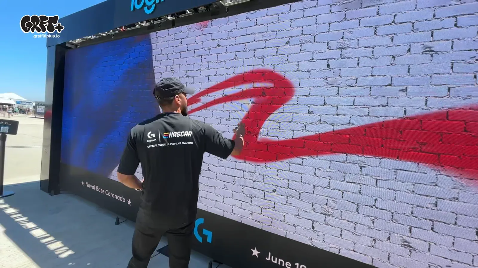 Graffiti+ resident artist spraying a bold red stroke live on the Logitech LED graffiti wall at NASCAR San Diego 2026