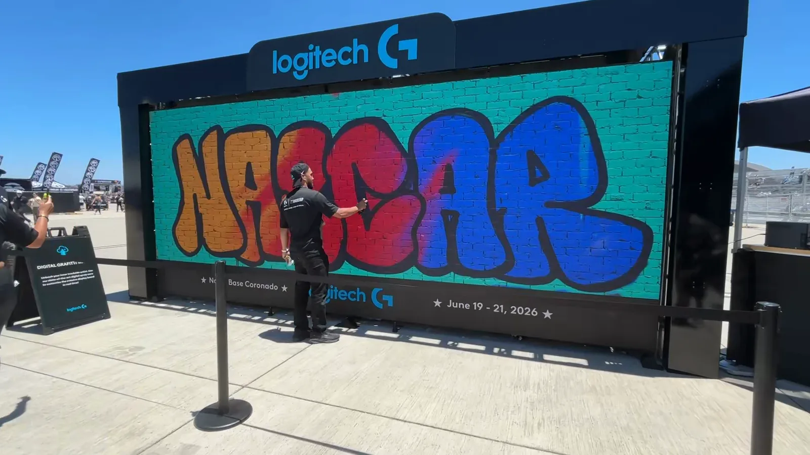 Graffiti+ resident artist painting a NASCAR throw-up on the Logitech 8x16 LED graffiti wall, trackside at NASCAR San Diego 2026
