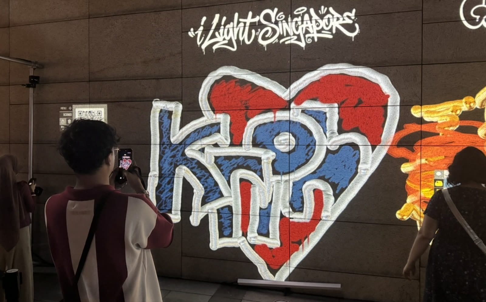 A visitor photographs a heart graffiti piece at i Light Singapore
