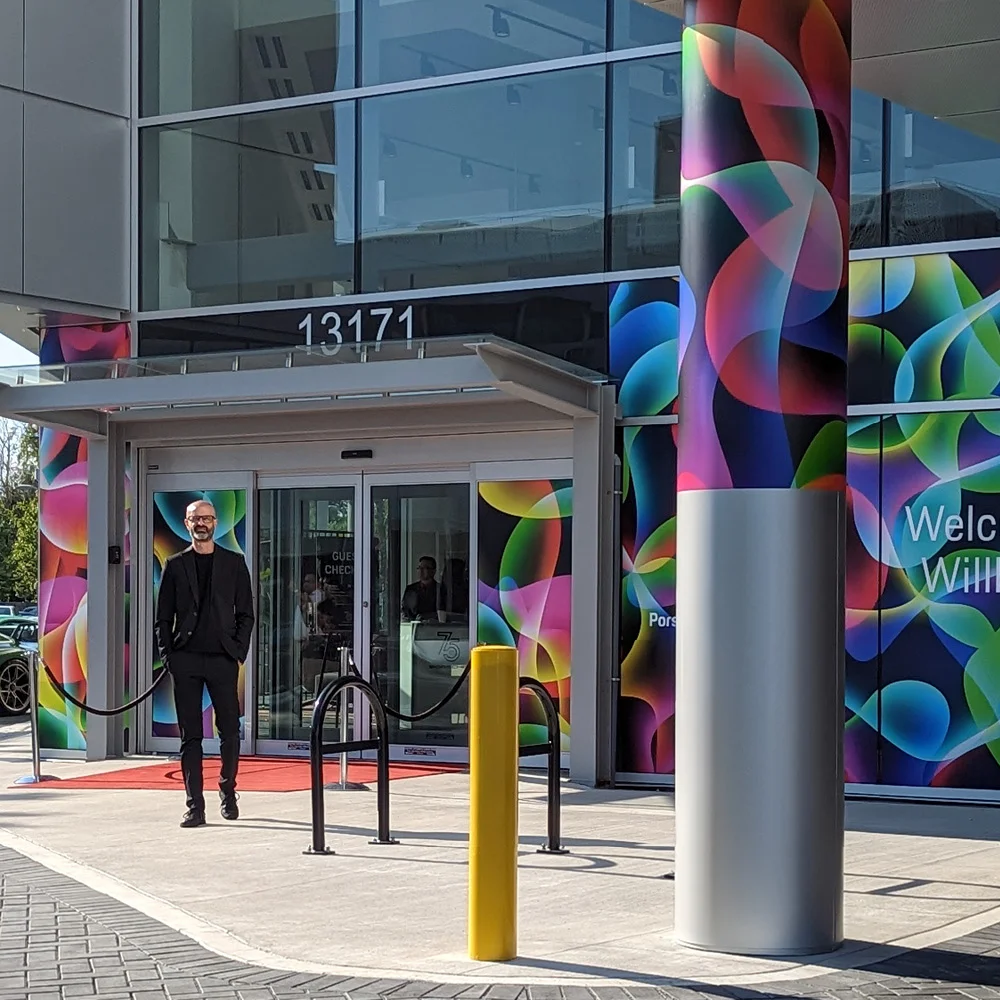 Carson Ting at the front entrance of Porsche Centre Richmond, with the building wrapped in the official Porsche 75th anniversary livery