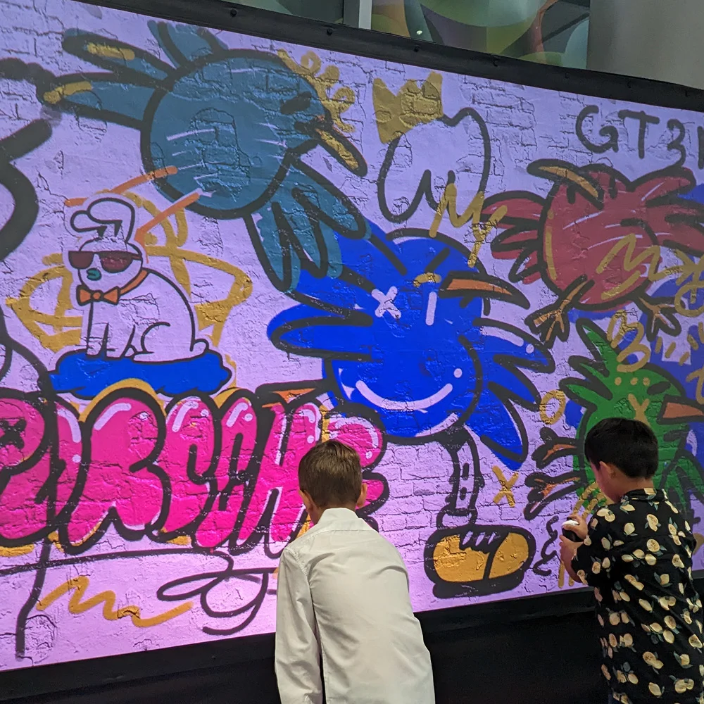 Two young guests painting Chairman Ting's character illustrations on the Graffiti+ LED wall at the Porsche 75th anniversary Festival of Dreams
